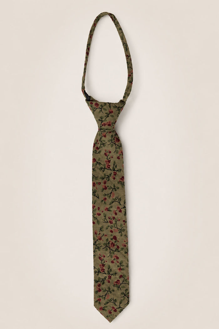 The Ivy City Co โTies in Woodland Floralโ showcases a khaki green cotton fabric adorned with a red and black woodland floral pattern. Displayed against a simple light background and tied in a classic knot with an adjustable loop, this tie is an understated yet charming wedding accessory.