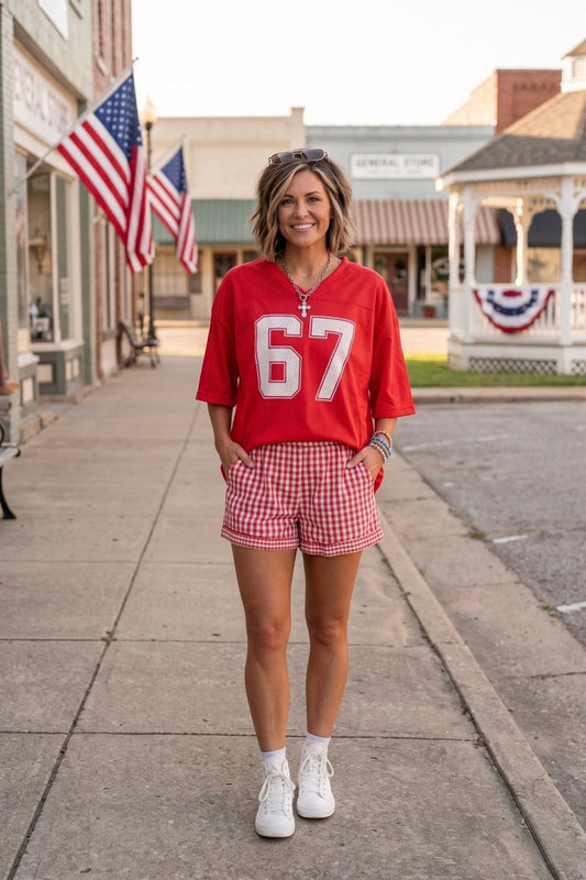 Red oversized Americana football jersey paired with red gingham shorts and white sneakers, styled as a casual Fourth of July outfit perfect for summer celebrations, country concerts, and patriotic weekend wear.