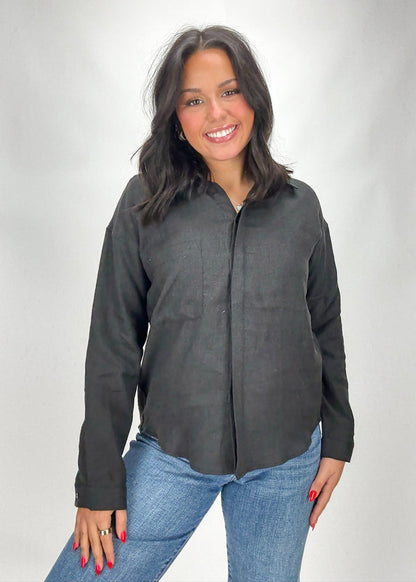 Woman wearing a dark gray button-up shirt and blue jeans on a white background