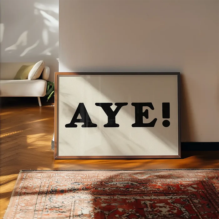 Aye Typography Poster Print framed, leaning on a wooden floor beside a rug
