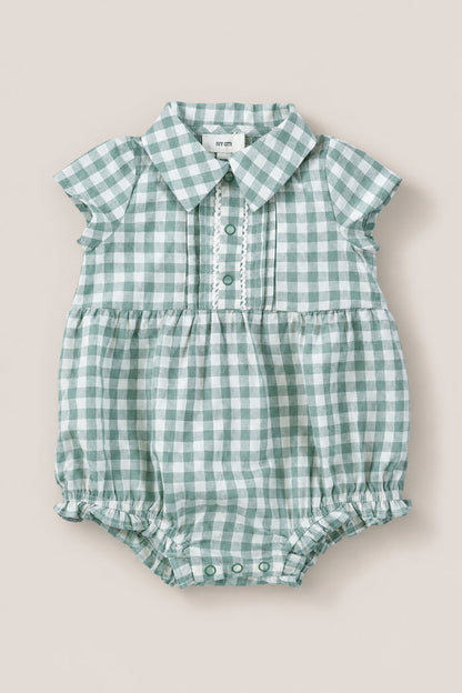 The Ivy City Co Baby Amber Romper in Sage Gingham features green and white cotton, short sleeves, a collar, button placket, and gathered leg openings. The vintage-inspired romper is shown laid flat on a neutral background.