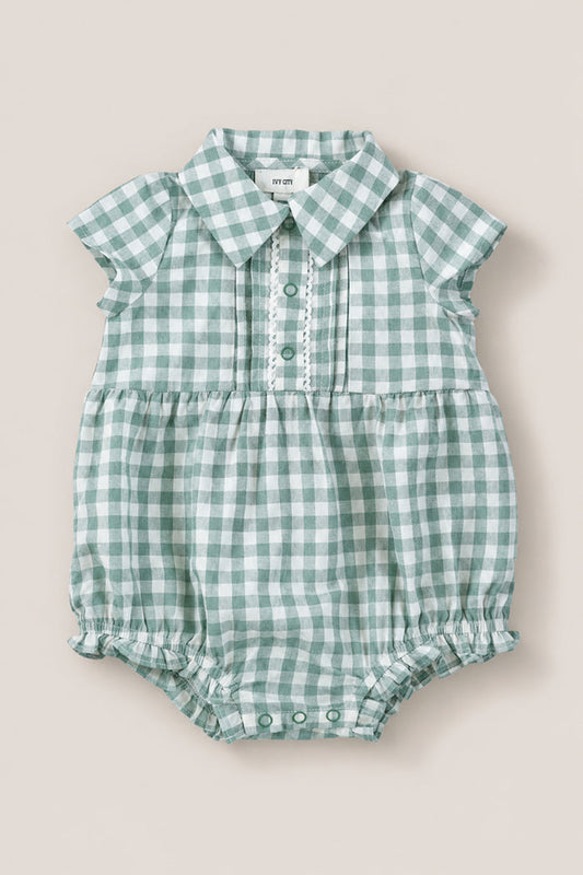 The Ivy City Co Baby Amber Romper in Sage Gingham features green and white cotton, short sleeves, a collar, button placket, and gathered leg openings. The vintage-inspired romper is shown laid flat on a neutral background.
