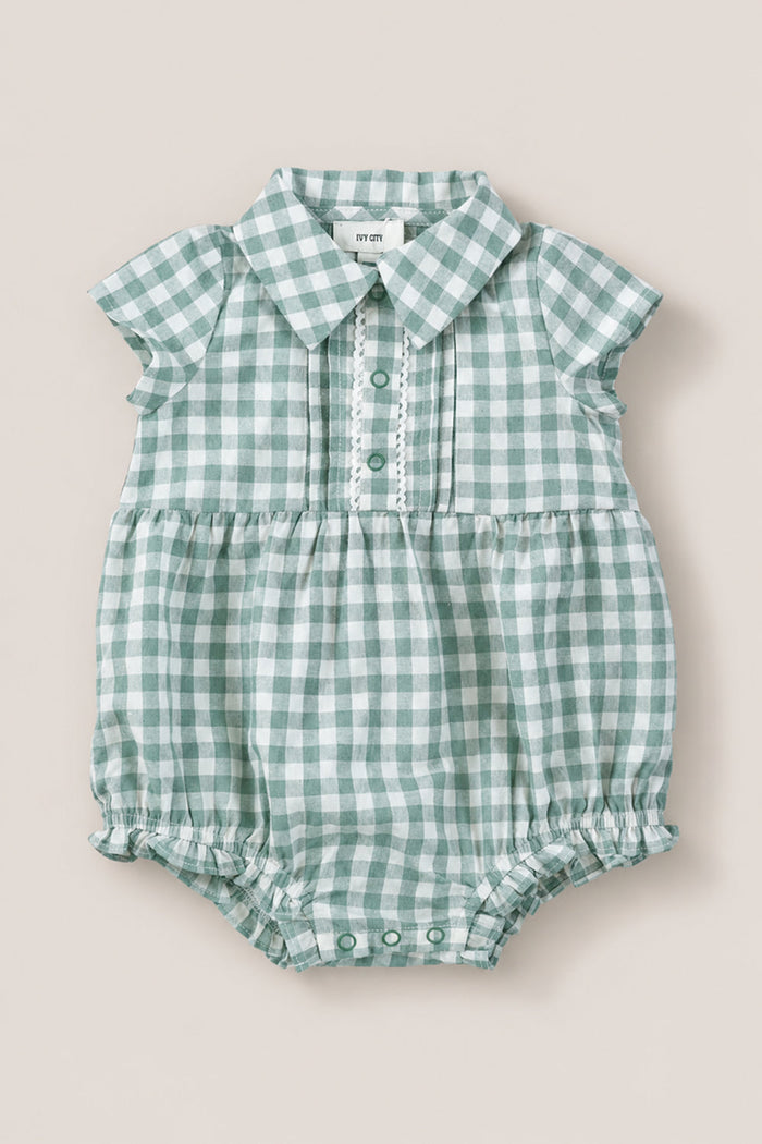The Baby Amber Romper in Sage Gingham by Ivy City Co features short sleeves, a collar, front buttons, and gathered leg openings. Made from 100% cotton for comfort and breathability.