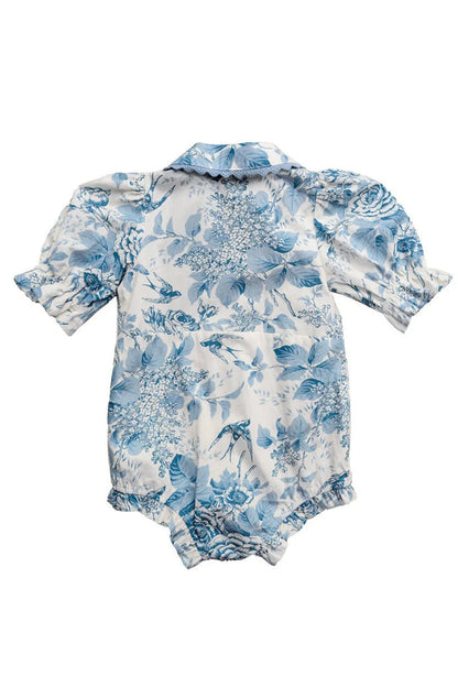 The Ivy City Co Baby Sophia Romper in Blue Floral features a delicate botanical print, short puff sleeves with ruffled trim, a collar, and ruffled edges at the legs.