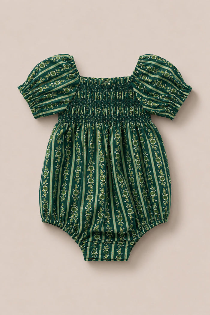 The Ivy City Co Baby Sunday Best Romper in Pine Felicity Floral features short puff sleeves, a gathered chest, and elastic leg openings. Crafted from fabric with vertical stripes and a delicate Pine Felicity Floral print, the romper is displayed on a beige background.
