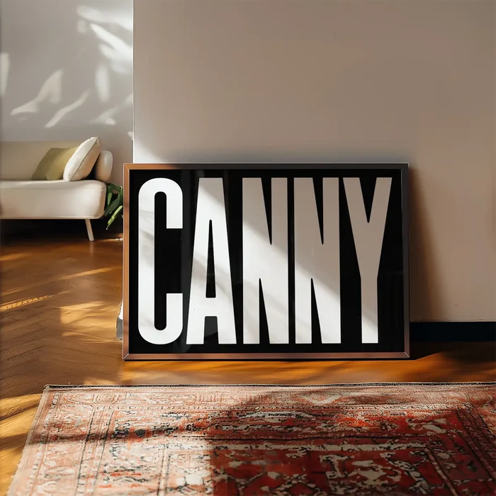 Canny Typography Poster Black and White Print framed, leaning on a wooden floor beside a rug