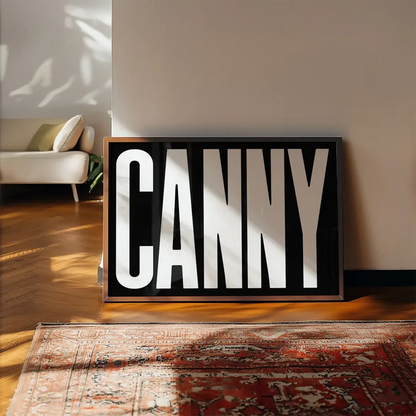 Canny Typography Poster Black and White Print framed, leaning on a wooden floor beside a rug