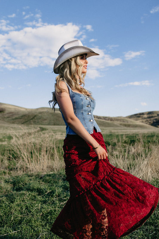 denim corset top styled with red lace maxi skirt and cowgirl hat, western country concert outfit, rodeo outfit idea, americana summer boutique fashion