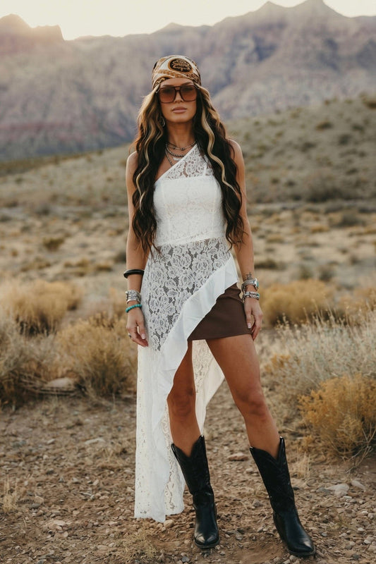 White one shoulder floral lace tunic top with an asymmetrical flowing hem paired with black wide leg pants.