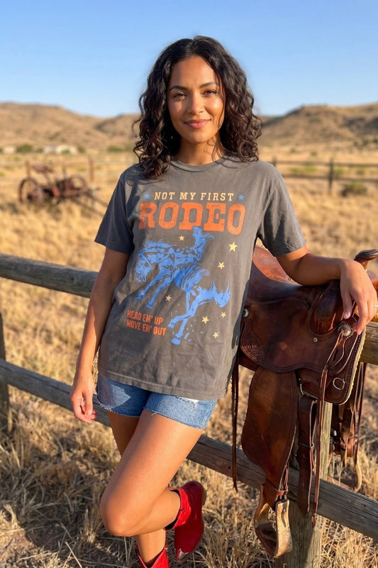 Vintage western graphic tee with "Not My First Rodeo" lettering and blue bucking horse illustration, styled for country concerts, rodeos, and cowgirl outfits.