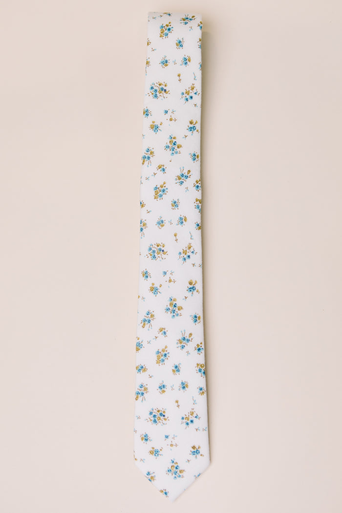 The Ivy City Co Ties in Madeline Blue Floral feature a white base with blue, yellow, and green floral accents—ideal for family matching—shown on a light beige background.