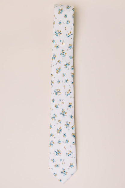 The Ivy City Co Ties in Madeline Blue Floral feature a white base with blue, yellow, and green floral accents—ideal for family matching—shown on a light beige background.
