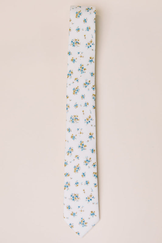 The Ivy City Co Ties in Madeline Blue Floral feature a white base with blue, yellow, and green floral accents—ideal for family matching—shown on a light beige background.