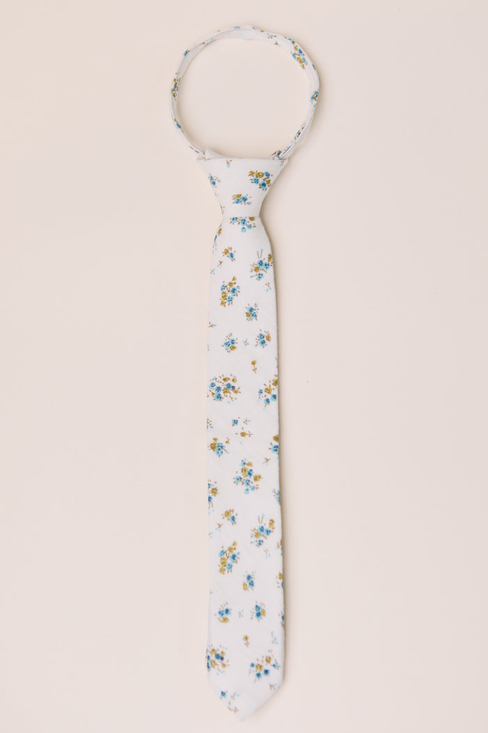 The Ties in Madeline Blue Floral by Ivy City Co feature a white base with blue and yellow flowers, shown flat on a beige background. Ideal for family matching or pairing with a boys bow tie.