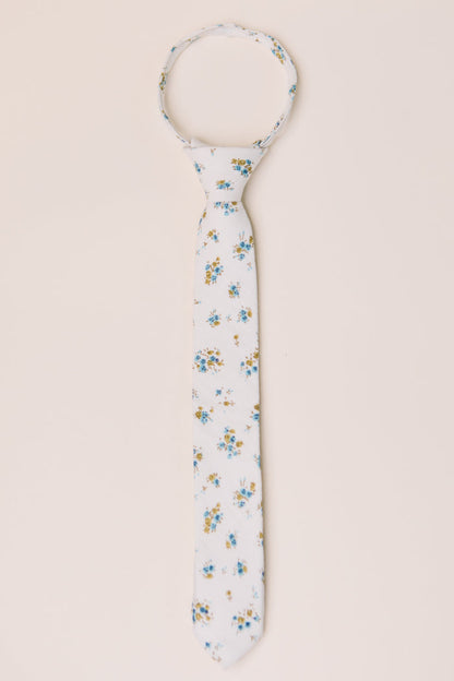 The Ties in Madeline Blue Floral by Ivy City Co feature a white base with blue and yellow flowers, shown flat on a beige background. Ideal for family matching or pairing with a boys bow tie.