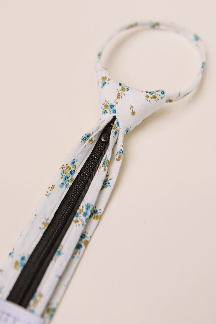 The Ivy City Co Ties in Madeline Blue Floral feature blue and yellow floral patterns on white, with a black zipper down the center—ideal for family matching or pairing with a boys bow tie.