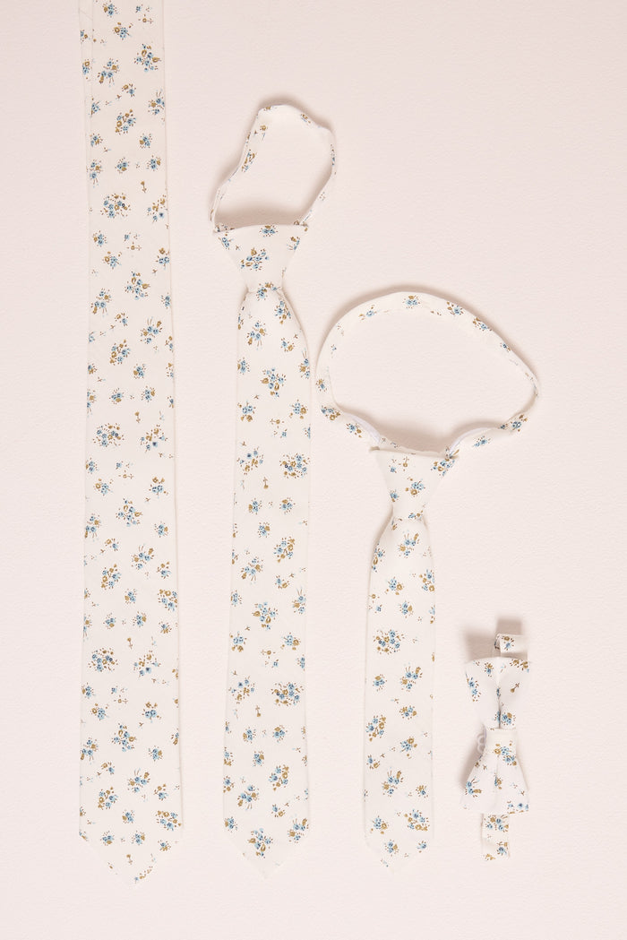Four Ivy City Co 'Ties in Madeline Blue Floral' are displayed on a light surface: adult, child, and baby ties, plus a boys' bow tie—all featuring delicate blue and yellow floral patterns for perfect family matching.