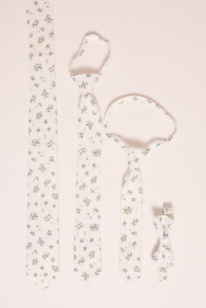 Four Ivy City Co 'Ties in Madeline Blue Floral' are displayed on a light surface: adult, child, and baby ties, plus a boys' bow tie—all featuring delicate blue and yellow floral patterns for perfect family matching.