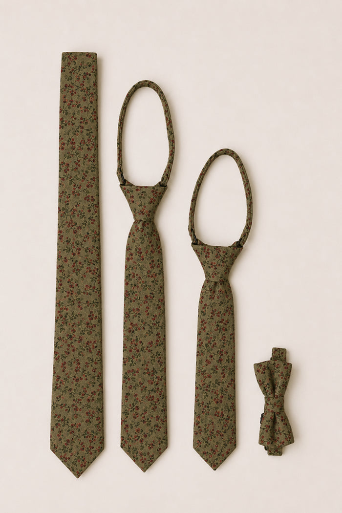 Four “Ties in Woodland Floral” by Ivy City Co—an adult necktie, child’s necktie, toddler’s necktie, and a bow tie—all made from soft cotton in an olive green shade with petite red woodland flowers, are arranged neatly on a light beige background. These coordinating accessories make the perfect charming woodland floral wedding set for the whole family.