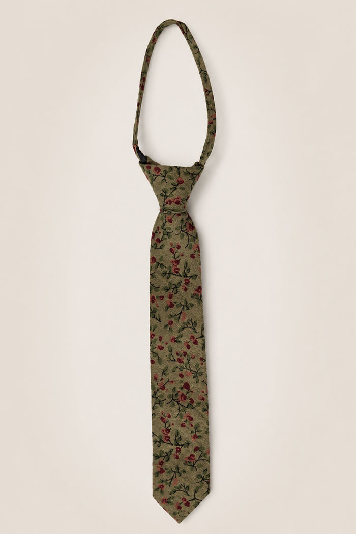 Ivy City Co's Ties in Woodland Floral features an olive green base adorned with a striking red and black floral motif, meticulously crafted from soft cotton—making it the perfect wedding accessory, showcased here against a simple light backdrop.
