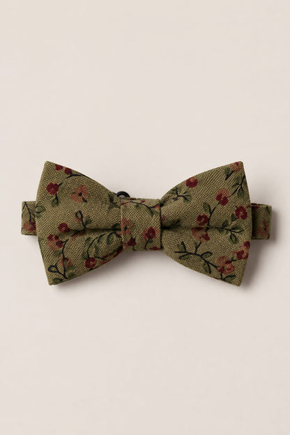 The Ties in Woodland Floral by Ivy City Co features an olive green bow tie adorned with a subtle Woodland Floral pattern of small red flowers and green leaves, crafted from soft cotton for a refined touch—an ideal wedding accessory showcased against a plain light background.