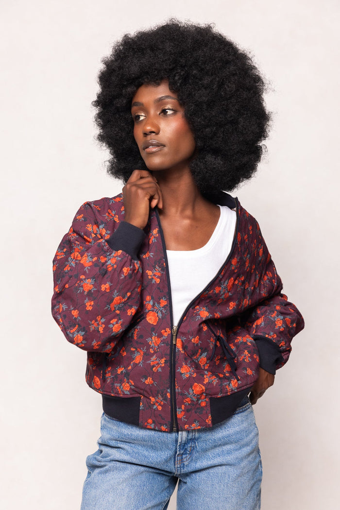 Woman wearing a floral bomber jacket and blue jeans against a plain background