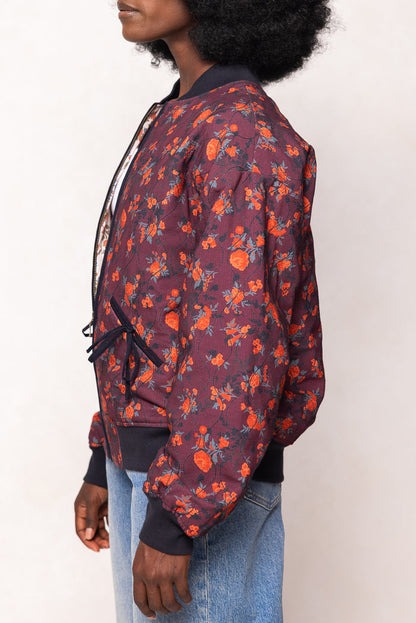 Person wearing a floral bomber jacket with orange flowers on a white background