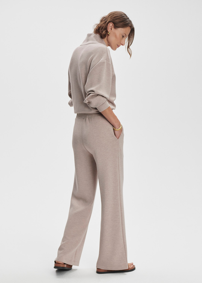 Woman turned to the side wearing taupe wide leg pants with a taupe half zip top against a white background