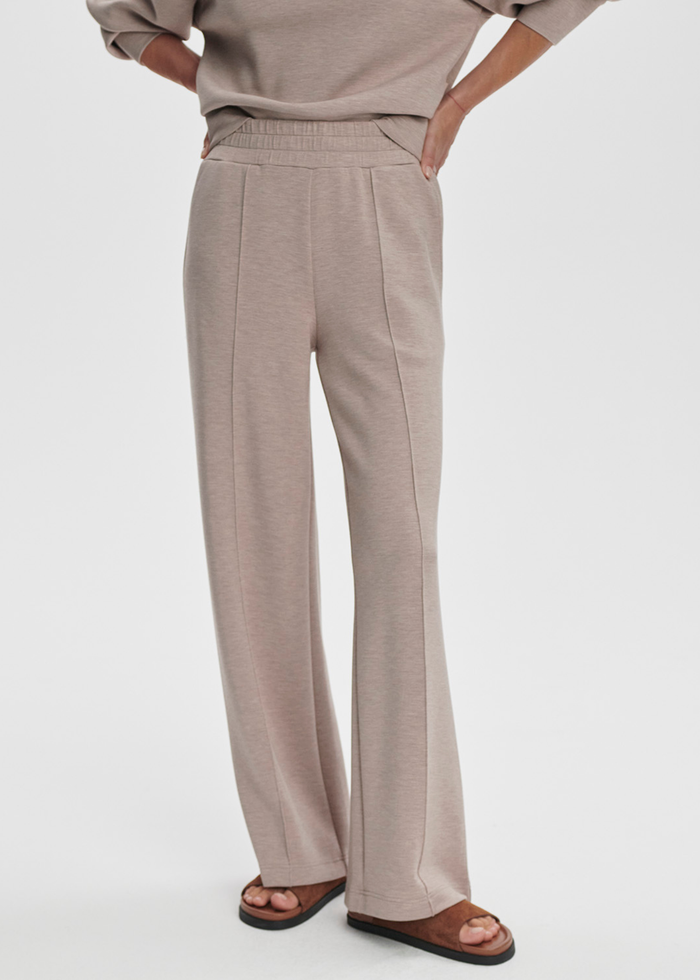Woman wearing taupe wide leg pants against a white background