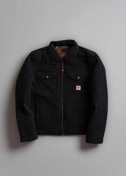 Black quilted jacket with plaid lining, buttoned pockets, and zipper, displayed on a gray background.