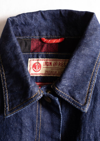 Close-up of a denim jacket collar with visible "Iron and Resin" label, featuring red plaid lining and contrast stitching.