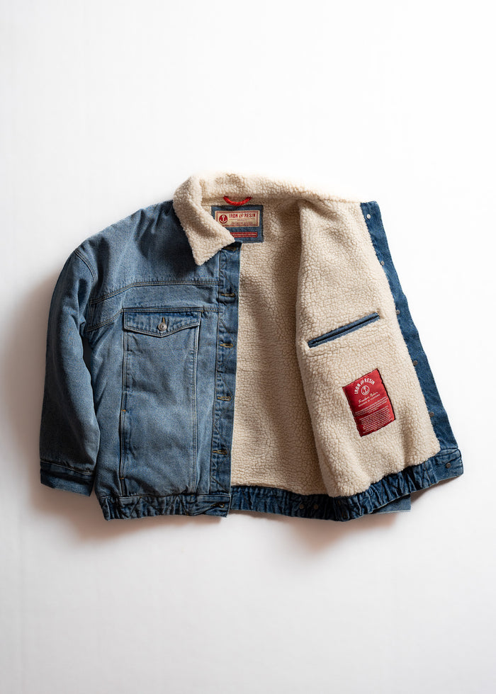 Denim jacket with sherpa lining, open to reveal red label inside. Features chest pocket and button details on a white background.