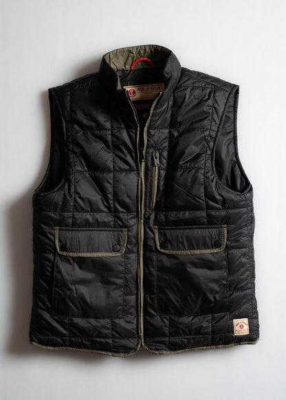 Black quilted vest with two front pockets and a zipper, featuring Iron & Resin branding on the collar, laid flat on a white surface.