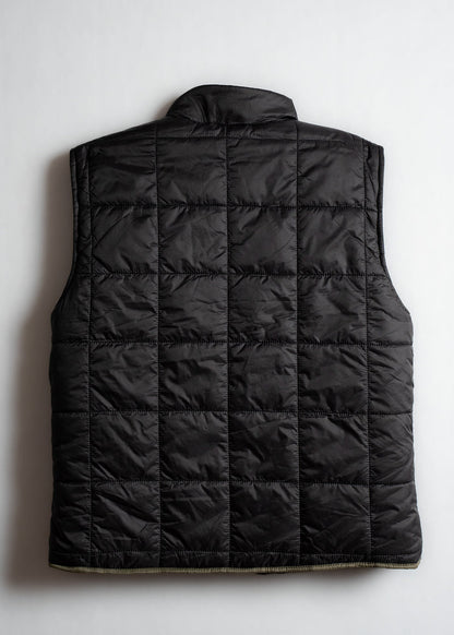 Black quilted vest with a high collar, viewed from the back, showcasing its square stitching pattern on a plain background.