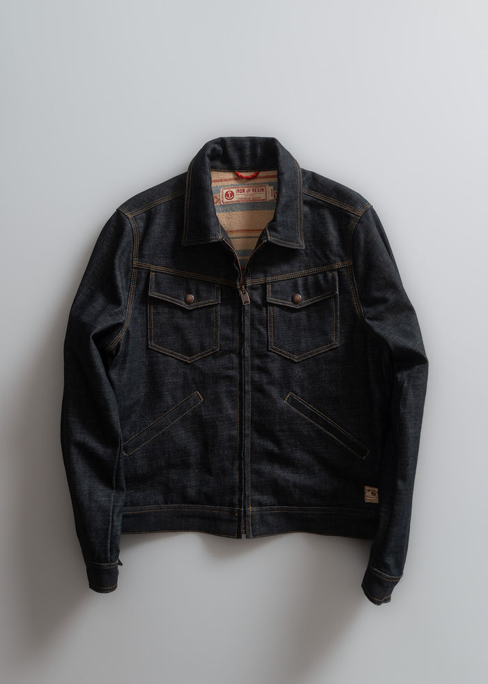 Dark denim jacket with brown stitching, two chest pockets, and a visible label, laid flat on a light gray background.