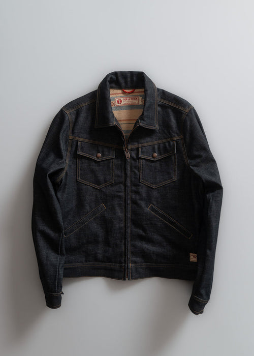 Dark denim jacket with brown stitching, two chest pockets, and a visible label, laid flat on a light gray background.