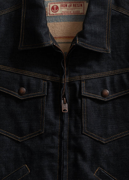 Close-up of a dark denim jacket with a zipper and two chest pockets. Label reads "Iron and Resin Premium Goods."