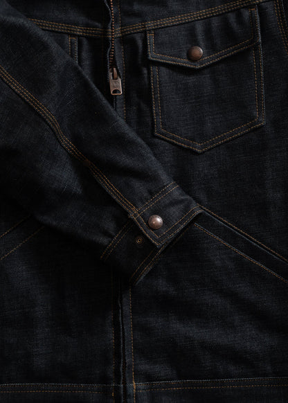 Dark denim jacket with brown stitching, featuring a front pocket, zipper, and metal buttons on the sleeve, showcasing detail.