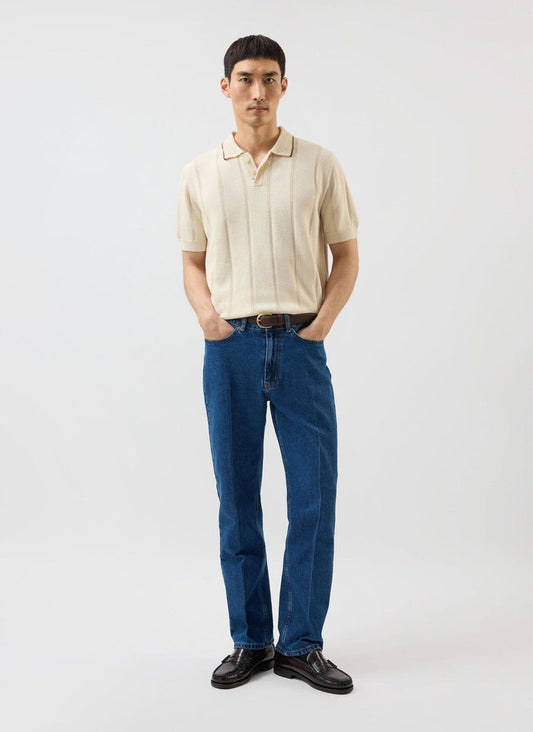 A model wears the Percival x Warren Wool Knitted Polo in ecru, styled with dark blue jeans and brown leather loafers.