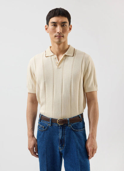 A man models the Percival x Warren ecru wool knitted polo with vertical stripes, tucked into blue jeans.