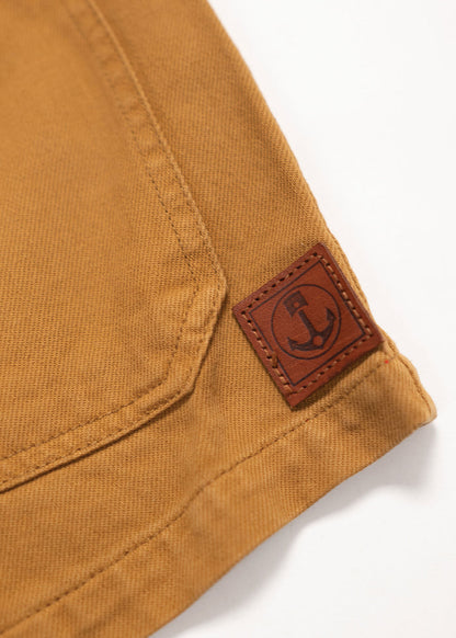 Close-up of a brown fabric corner with a stitched seam and a leather patch featuring an anchor logo, set against a white background.
