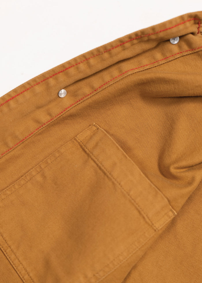Close-up of a brown fabric with red stitching and metal rivets, showcasing a pocket detail on a garment.