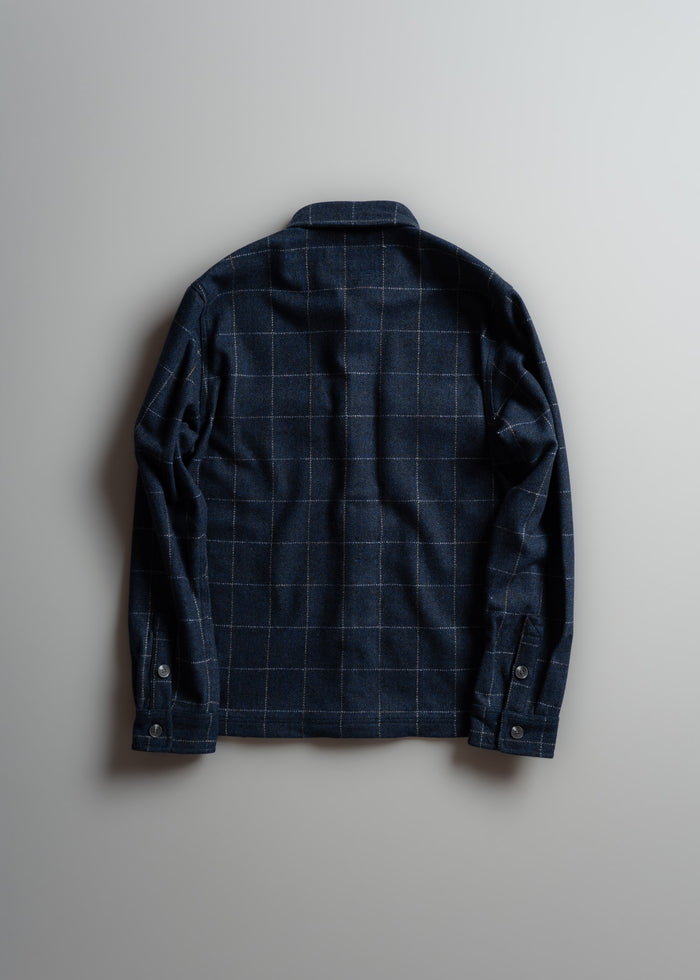 A navy blue plaid shirt with buttoned cuffs is laid flat on a light gray background, showcasing its back design and pattern.