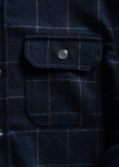 Close-up of a blue plaid wool shirt pocket with a button, showcasing the fabric's texture and pattern in detail.
